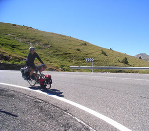 Jeff Boggess cycling on a mountain road with green hills and clear blue sky.